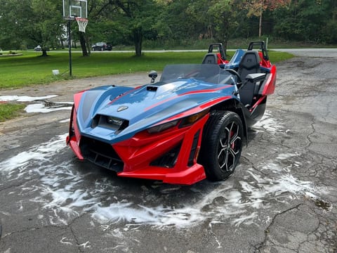 Front three-quarter view of a red and blue Polaris Slingshot after an exterior hand wash, nose and front wheel clean